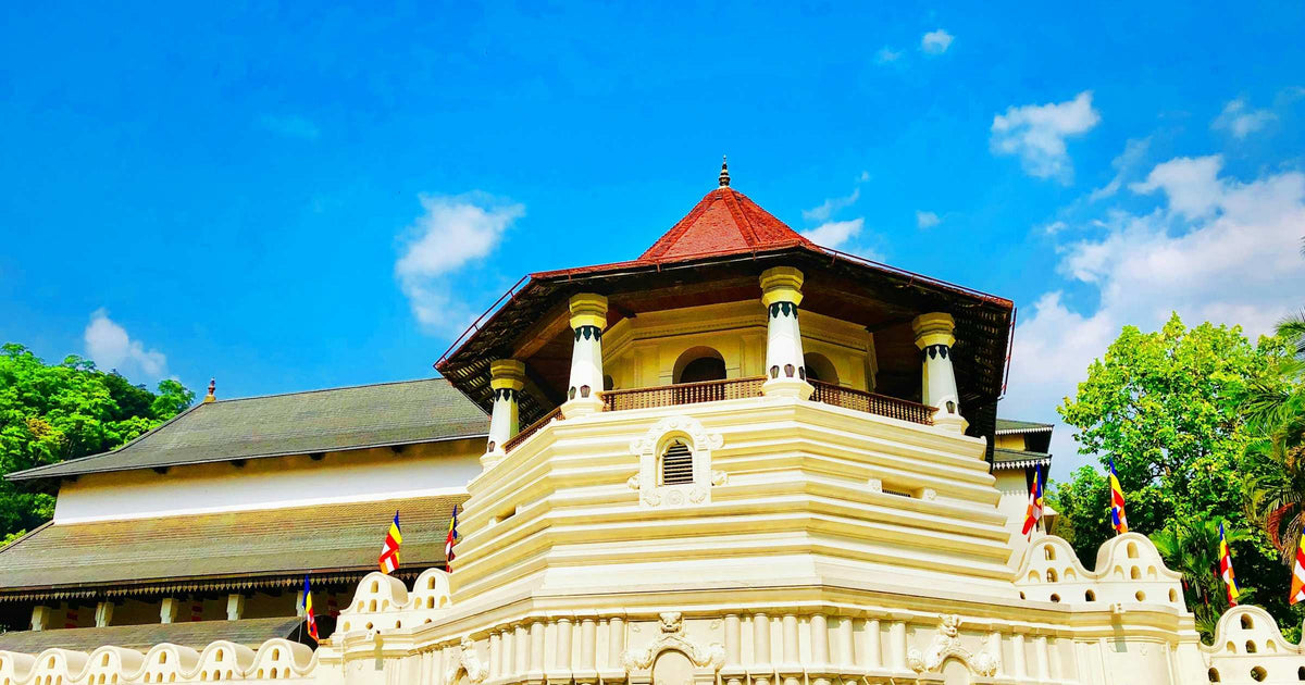 The Temple of the Tooth Relic in Kandy, Sri Lanka, gleaming white under a blue sky with Buddhist flags