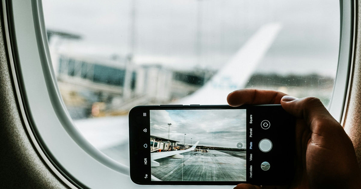 Traveller holding iPhone at airplane window checking phone settings before Asia trip