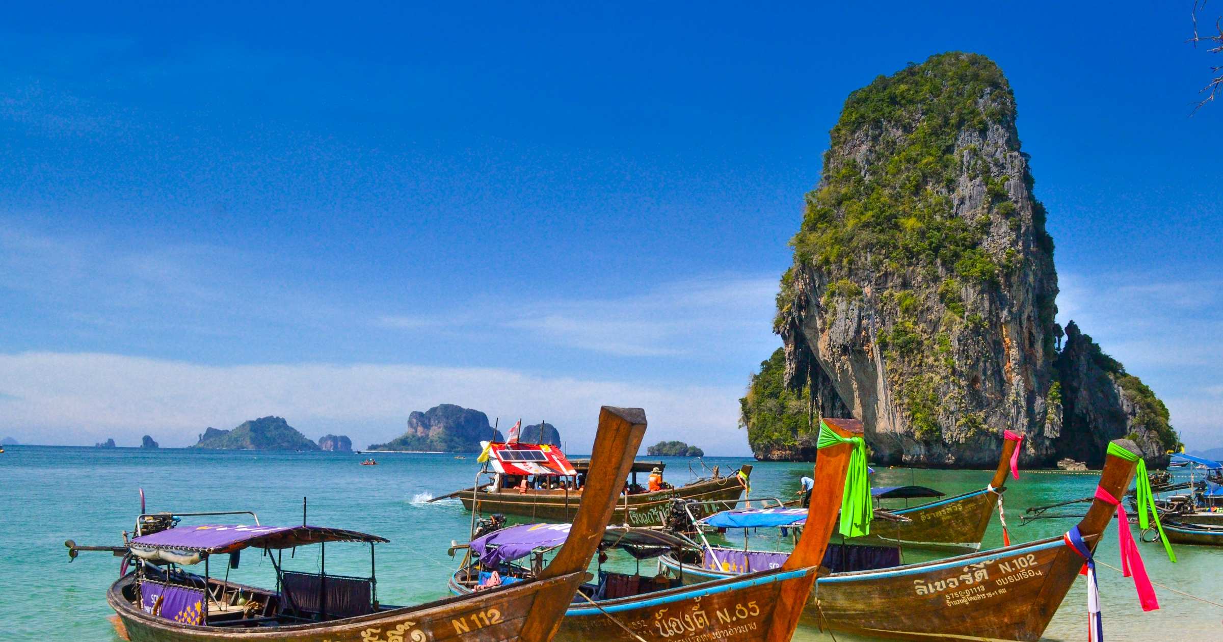 Longtail boats on turquoise water at Railay Beach, Thailand with limestone karst cliffs