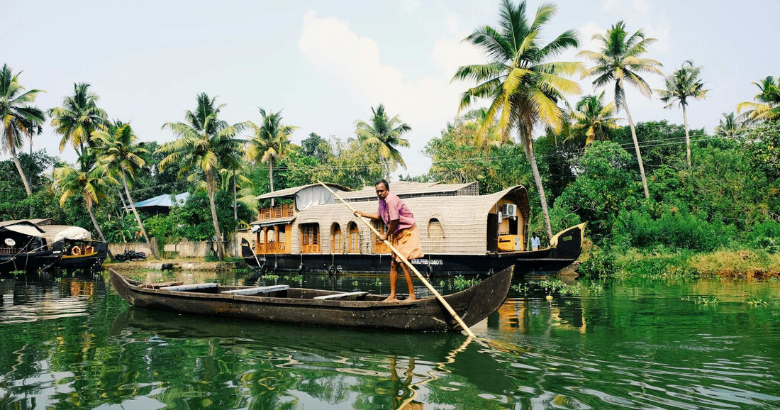 Traditional boatman on the Kerala backwaters near Alleppey, India, with a houseboat and palm trees