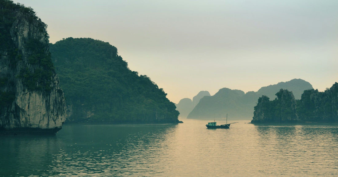 Ha Long Bay limestone karst scenery at dusk in Vietnam, with a traditional boat on calm water